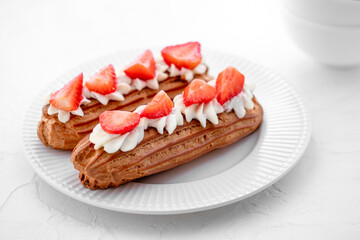 Eclairs with cream and strawberries on a white plate. 
