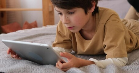 Boy using digital tablet lying on bed at home