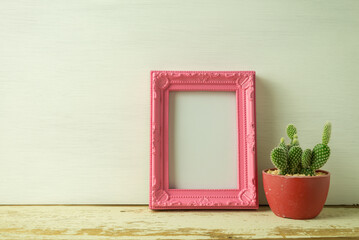 Vintage pink photo frame on old wooden table with cactus over white wooden background. Lifestyle and home decoration concept.