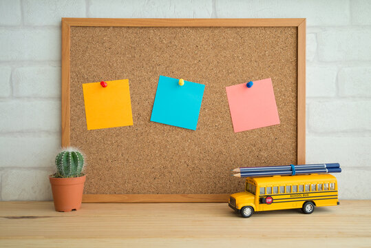 Black to school, education concept. Color paper attach on cork board and bus school toy with pencils on wooden table over white brick wallpaper background.
