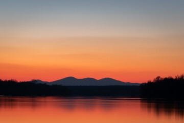 Fototapeta na wymiar Landscape of Sava river, forest and distant mountain silhouettes, clear sky with vibrant red and orange glow at horizon during twilight