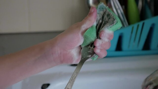 Children's hands wash a fork in a white sink with a sponge with foam