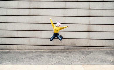 Female wearing vibrant unicorn mask jumping against wall