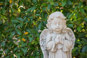 White cute cupid statue in garden with green tree background. Love valentine day concept.