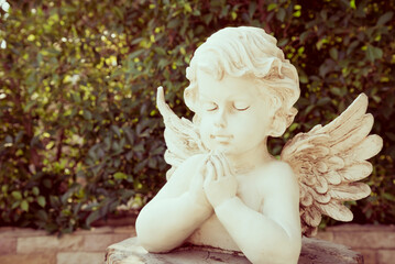 White cute cupid statue in garden with green tree background. Love valentine day concept.