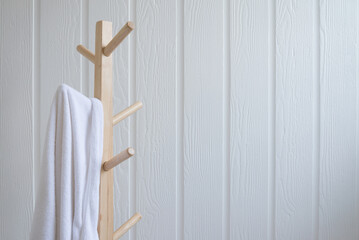White towel hanging on wooden cloth hanger rack with white wall background copy space.