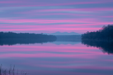 Peaceful atmospheric landscape with pastel colors, Sava river at twilight, forested banks lead to distant mountain silhouette in haze, calm nature and water reflection in long exposure