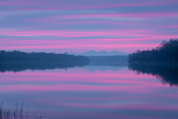 Peaceful atmospheric landscape with pastel colors, Sava river at twilight, forested banks lead to distant mountain silhouette in haze, calm nature and water reflection in long exposure © slobodan