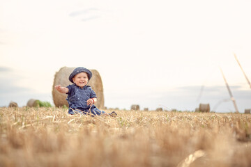 Naklejka na ściany i meble Little happy girl on a gold wheat field at sunset.