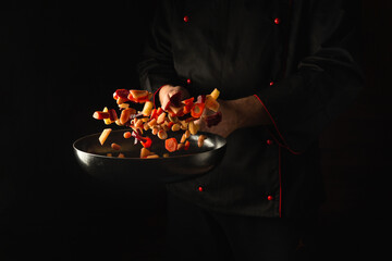 The chef prepares fresh vegetables in a frying pan. Grande cuisine and food recipe on dark background. Free advertising space