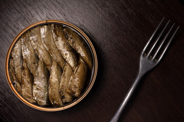 close-up photo of canned fish - sprats in oil and a retro fork - on a dark wooden background