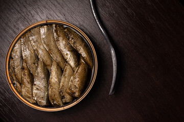 photo of canned sprats in oil and an fork gracefully repeating the bend of the can on a dark wooden background