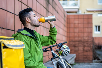 Young delivery man having rest, fast express delivery service worker drinking water from his flask,...