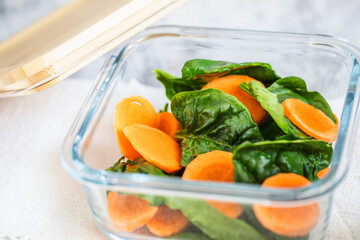 Glass boxes with fresh raw vegetables. Carrots and spinach. Vegan food and snacks in containers, gray background.Clean eating, vegetarianism, raw food, detox, plant based diet concept.