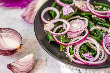 Fresh healthy vitamin salad. Salad of red onion, spinach and blue Chinese cabbage, seasoned with olive oil and sesame seeds. Close-up with focus on onion rings.Healthy food. Vegan food. Raw food  