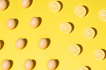 Pattern made of eggs and lemon slices. Sharp shadow. Yellow background. Simple Easter concept. Flat lay. 