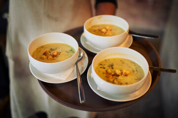 Here comes the starters. Closeup of an unrecognizable waiter holding a tray of soup that hes about to serve to customers inside of a restaurant during the day.