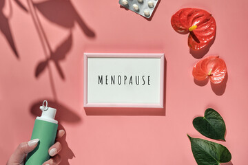 Menopause, text in pink frame. HRT Replacement hormone therapy concept. Pink background with exotic leaves, flowers, pills, estrogene gel in hand. Sunlight, long floral shadows. - obrazy, fototapety, plakaty