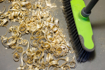 a small pile of wood shavings on a gray linoleum floor with a broom brush