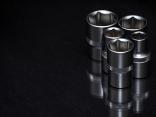 Ratchet wrench. Set of stainless steel hex sockets on shiny black surface. Universal professional tool for car repair. Low key photo.