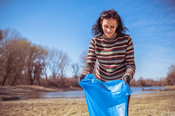 woman carrying blue garbage bag and cleaning the environment