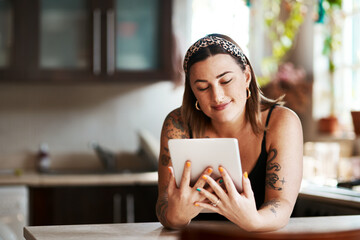 Theres a lot we can relate to on social media. Shot of a young woman using a digital tablet in the kitchen at home.