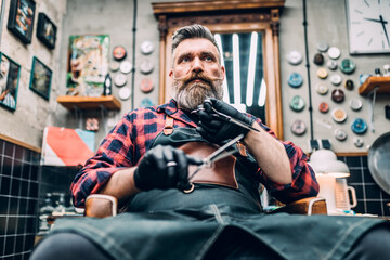 Portrait of midlle-aged barber sitting on chair in his barber shop.