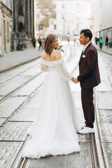 Naklejka na ściany i meble An international wedding couple, a European bride and an Asian groom walk around the city together.