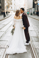 Naklejka premium An international wedding couple, a European bride and an Asian groom walk around the city together.