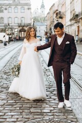 Naklejka premium An international wedding couple, a European bride and an Asian groom walk around the city together.