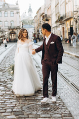 Naklejka premium An international wedding couple, a European bride and an Asian groom walk around the city together.