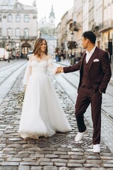 Naklejka premium An international wedding couple, a European bride and an Asian groom walk around the city together.