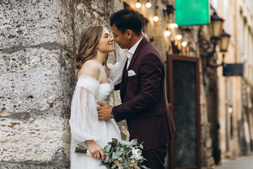 An international wedding couple, a European bride and an Asian groom walk around the city together.