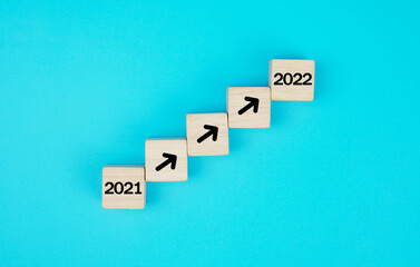Wood block stacking as step stair.  business growth success process with arrow moving up from year 2021 to 2022, on blue background.               