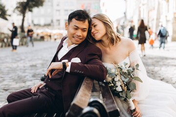Fototapeta premium An international wedding couple, a European bride and an Asian groom walk around the city together.