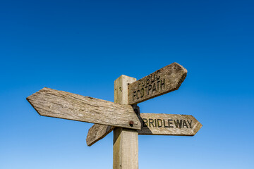 Multidirectional wooden signpost showing public footpaths and bridleways in the rural countryside