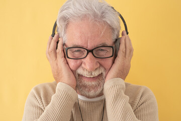 Smiling white-haired senior man wearing black headphones listening music looking at camera. Attractive bearded elderly grandfather with hands on headphones enjoying technology