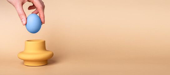 Blue dyed Easter egg in stand with beige copy space on banner.