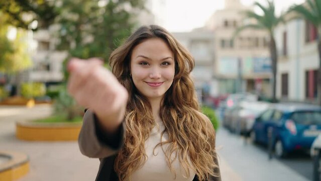Young hispanic woman smiling confident doing coming gesture with finger at street