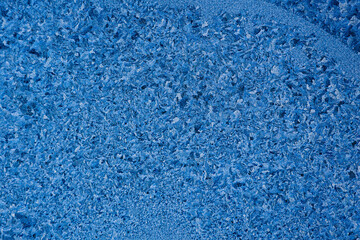 Pattern or pattern of frost and snowflakes on frozen glass of window. Christmas back. Macrophotography. Flat empty snow-covered surface of blue color.