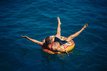 A young man floats on an inflatable air ring circle in the sea with blue water. Festive holiday on a happy sunny day.