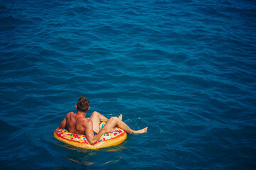 A young man swims in the open sea on an inflatable ring on a sunny day. Summer vacation, tourist on vacation