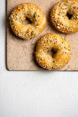 Three bagels with seeds on a baking stone on a concrete white background with a copy space top view. Healthy bread buns for breakfast.