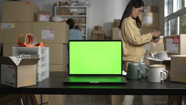 Laptop with blank green screen standing on the desktop in the warehouses. E-commerce business owner working in store warehouse.