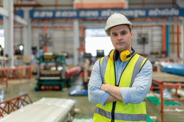Portrait of male engineer wearing safety vest with white helmet standing arms crossed in factory....