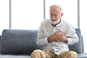 senior elderly man chest pain or suffering from heart attack on a sofa