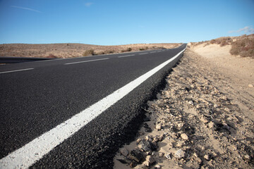 Lange gerade Landstraße in einer kargen, trockenen Landschaft, Perspektive vom Fahrbahnrand aus