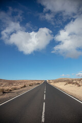 Einsame gerade Straße in einer öden Landschaft auf Fuerteventura. Mit einem sonnigen Himmel und Schönwetter-Wolken