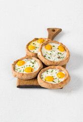Open mini rye cottage cheese pies with mozzarella, quail eggs and dill, on a wooden board. Light background