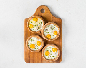 Mini open pies with mozzarella, quail eggs and dill, on a serving wooden board. Light background. Top view